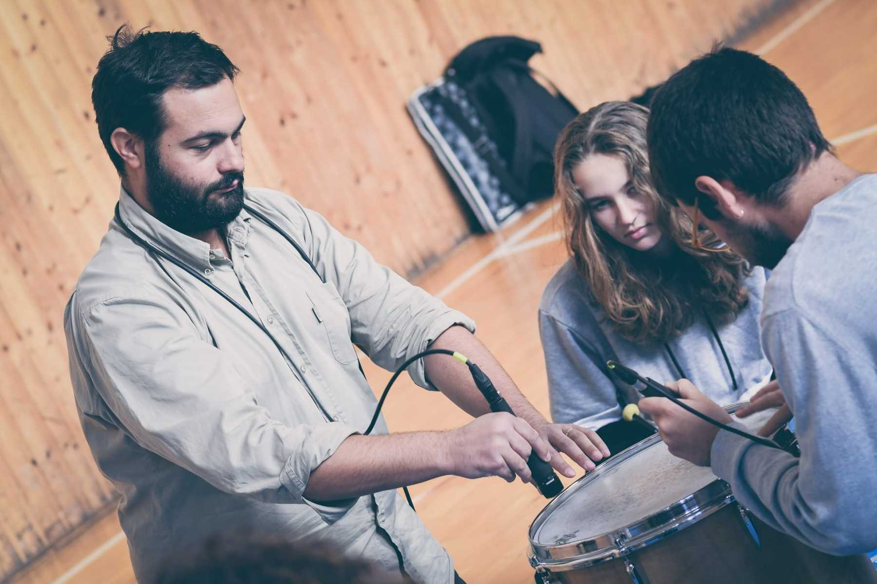 Umělec se dvěma studenty pracují s mikrofony a bicími nástroji.